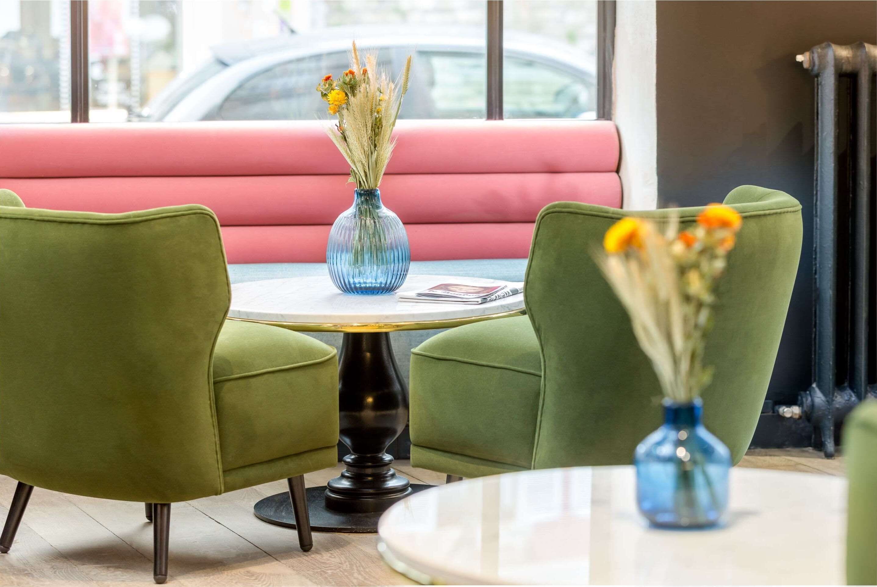 A seating area with green chairs and a table, a vase with flowers, and a pink cushioned bench.