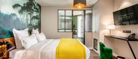 Una habitación de hotel moderna con una cama grande, una manta amarilla, un televisor, un escritorio con lámpara y una silla verde.