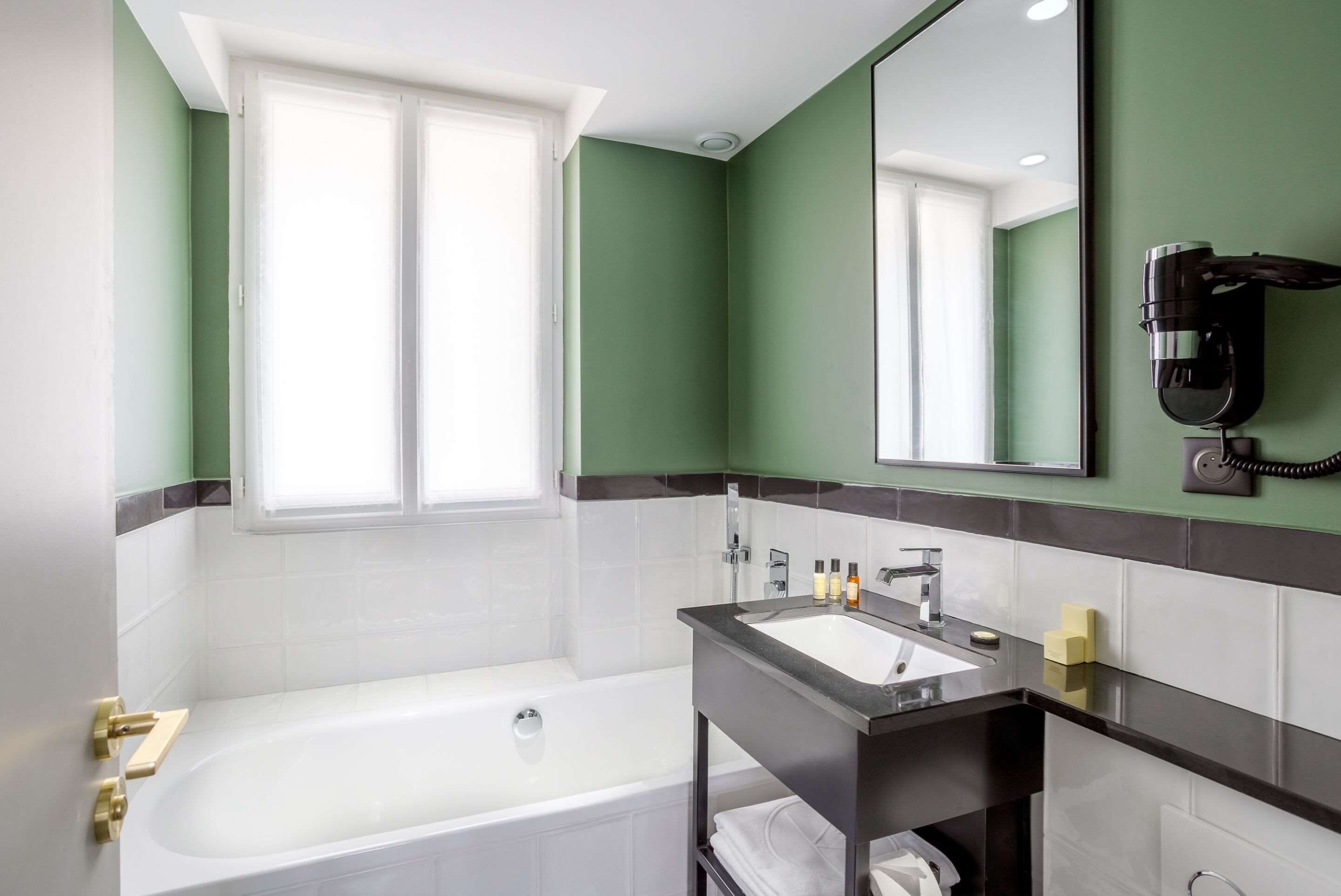 Een moderne badkamer met een badkuip, een wastafelmeubel en een haardroger bevestigd aan de muur.