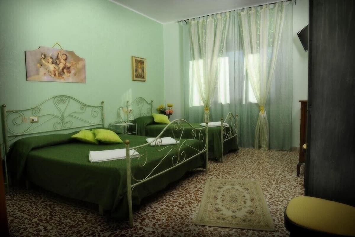 A room with two beds, green bedding, a patterned carpet, and a window with sheer curtains.