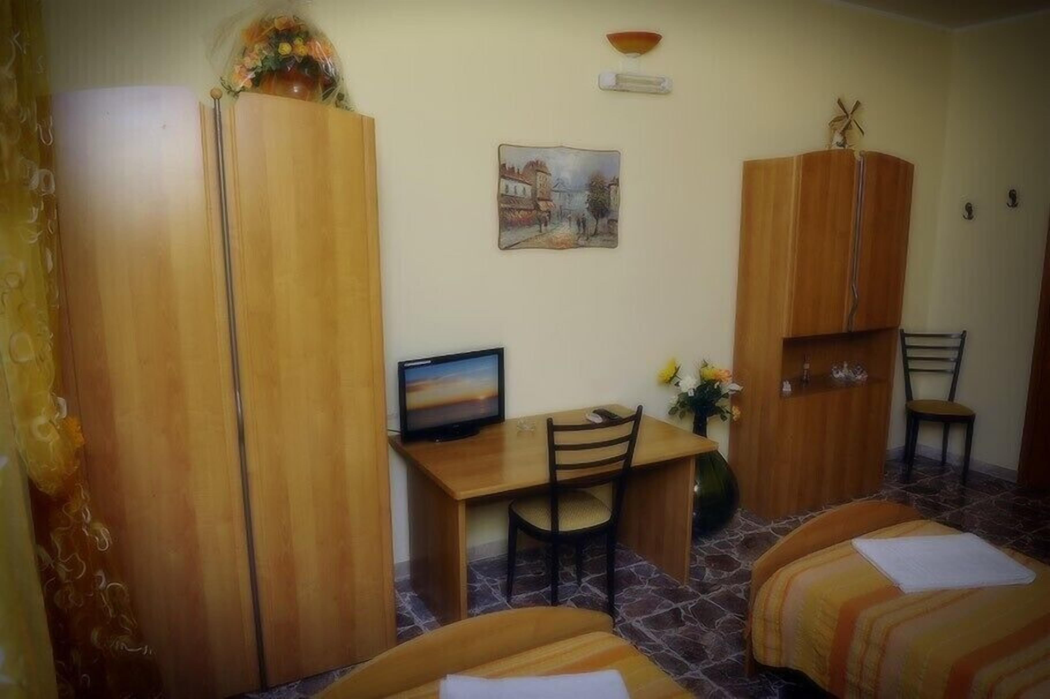 Una habitación pequeña y acogedora con un escritorio de madera, una silla, una cama con manta a rayas y un televisor.