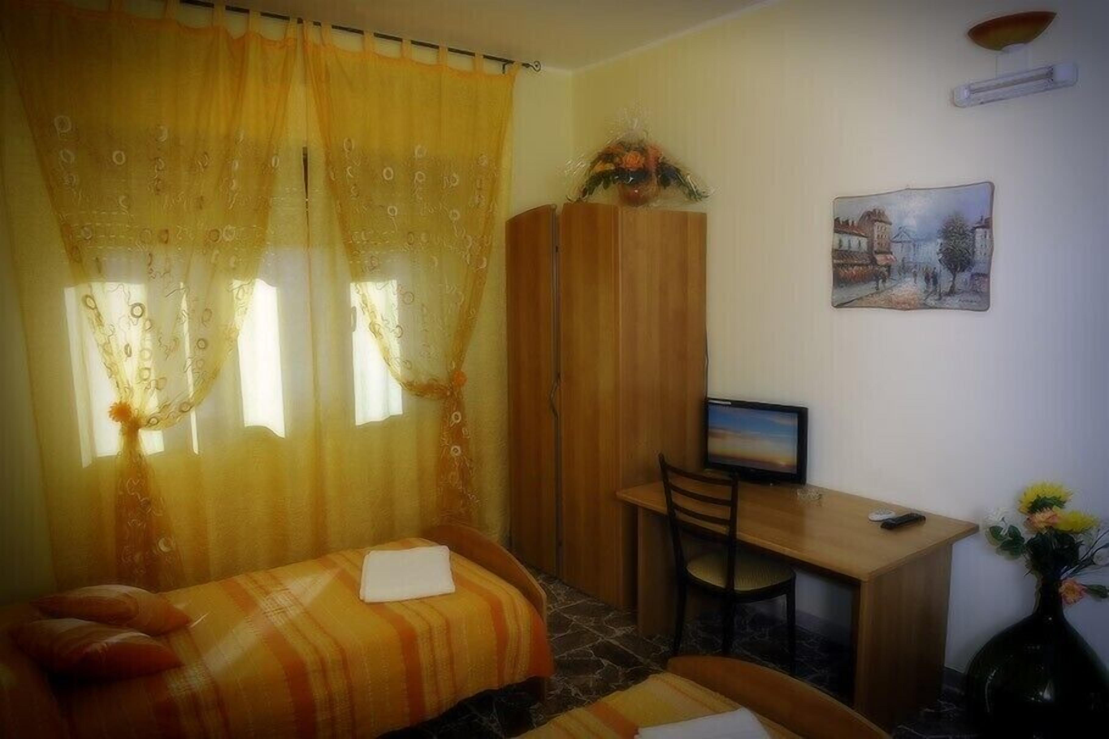 Una stanza con un letto, una scrivania, una sedia, una televisione e un quadro appeso al muro.