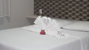 A neatly made bed with white linens and a decorative swan arrangement, a tufted headboard, and a bedside table with a lamp. - Xingu Praia Hotel (Altamira)