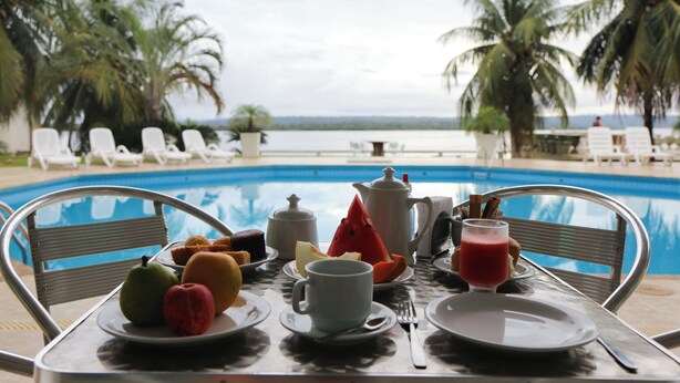 A table with breakfast items and a view of a pool and palm trees. - Xingu Praia Hotel (Altamira)