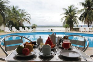 Una mesa con alimentos para el desayuno y vistas a una piscina y palmeras.