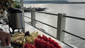 A table with fruit and a water dispenser on a balcony overlooking a body of water. - Xingu Praia Hotel (Altamira)