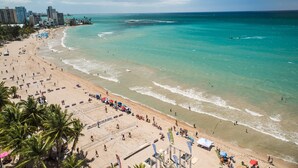 Una playa con aguas turquesas cristalinas, una orilla arenosa y un horizonte urbano al fondo.