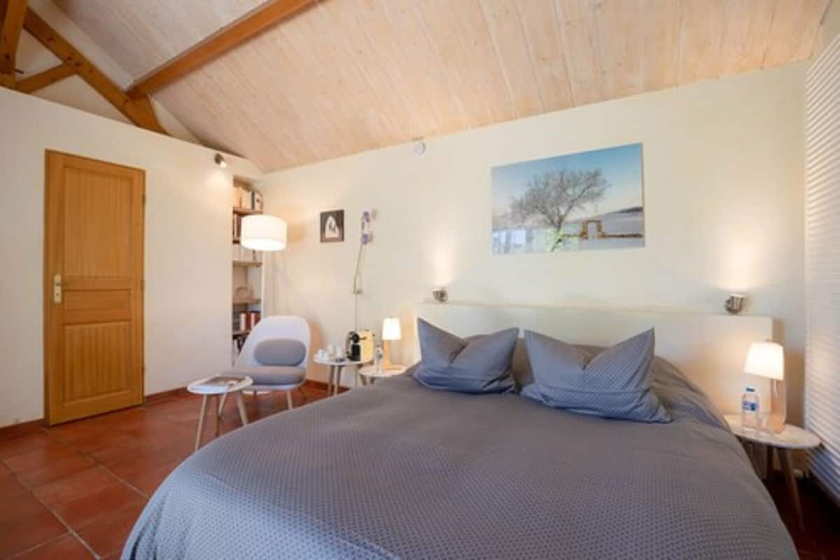 Une chambre à coucher avec un grand lit, une chaise, une petite table et une table de chevet avec une lampe.