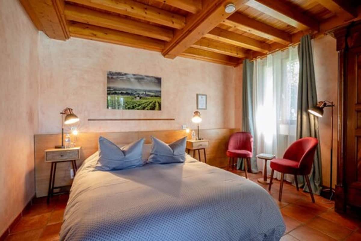 Une chambre à coucher avec un grand lit, deux tables de chevet avec des lampes, un fauteuil rouge et une fenêtre avec des rideaux.