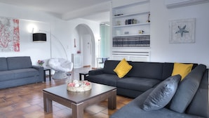 A modern living room with a grey sofa, a coffee table, and a bookshelf. - Athens Glyfada Riviera Apartment (Glyfada)