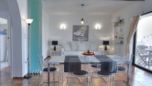 A modern dining area with a glass table, metal chairs, and a central island with a fruit bowl. - Athens Glyfada Riviera Apartment (Glyfada)