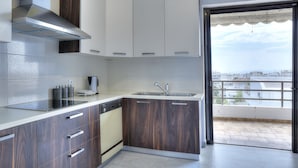 A modern kitchen with a dishwasher, stove, and a view of the city through a balcony. - Athens Glyfada Riviera Apartment (Glyfada)