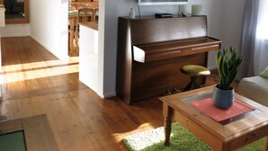 Una sala de estar con un piano de madera, un televisor de pantalla plana, un comedor con muebles de madera y una alfombra verde.