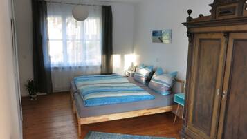 Ein Schlafzimmer mit einem Holzbett, einem Nachttisch, einer Lampe, einem Kleiderschrank und einem Fenster mit Vorhängen.