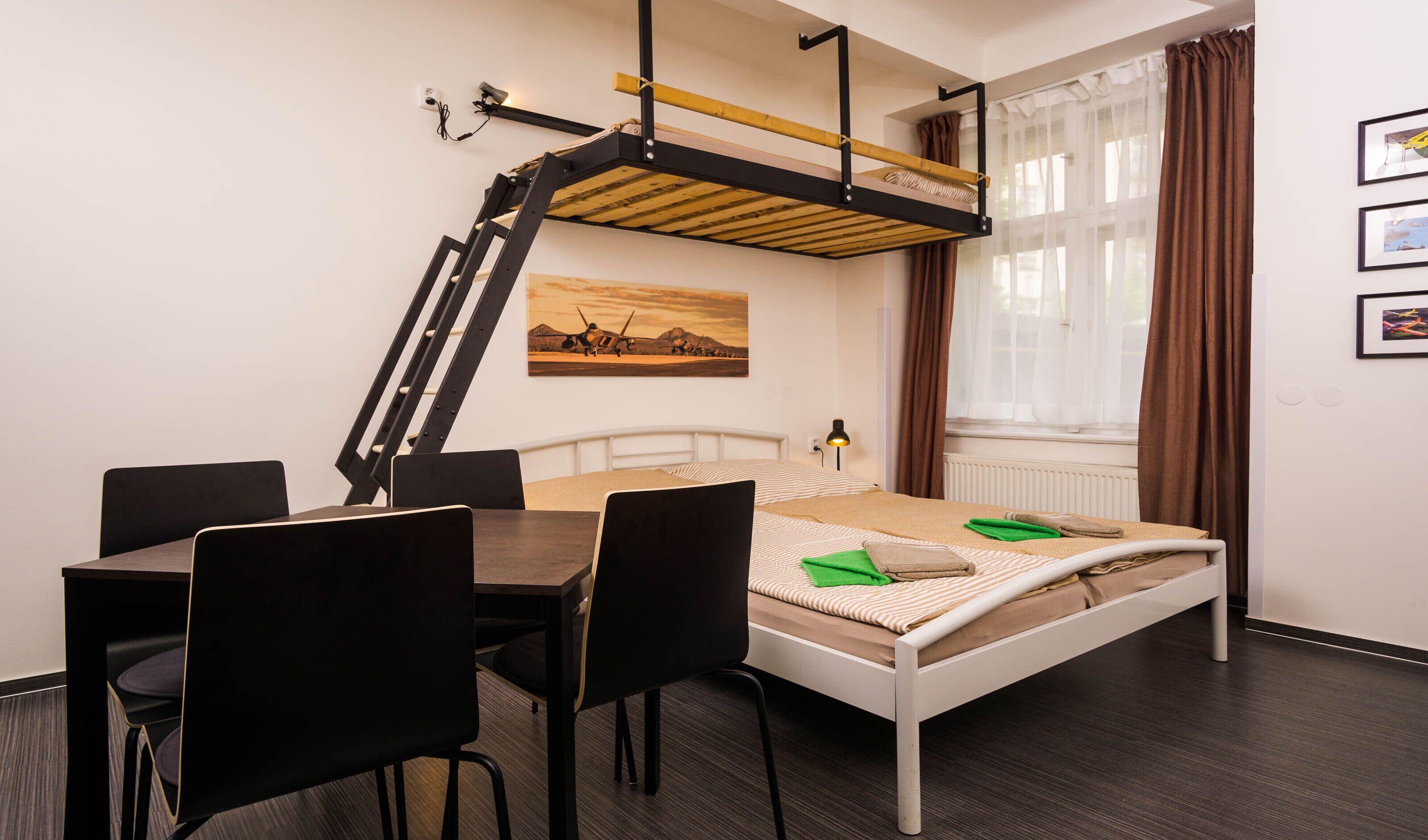 A compact hotel room with a bunk bed, a desk with chairs, a small table, and a window with curtains.