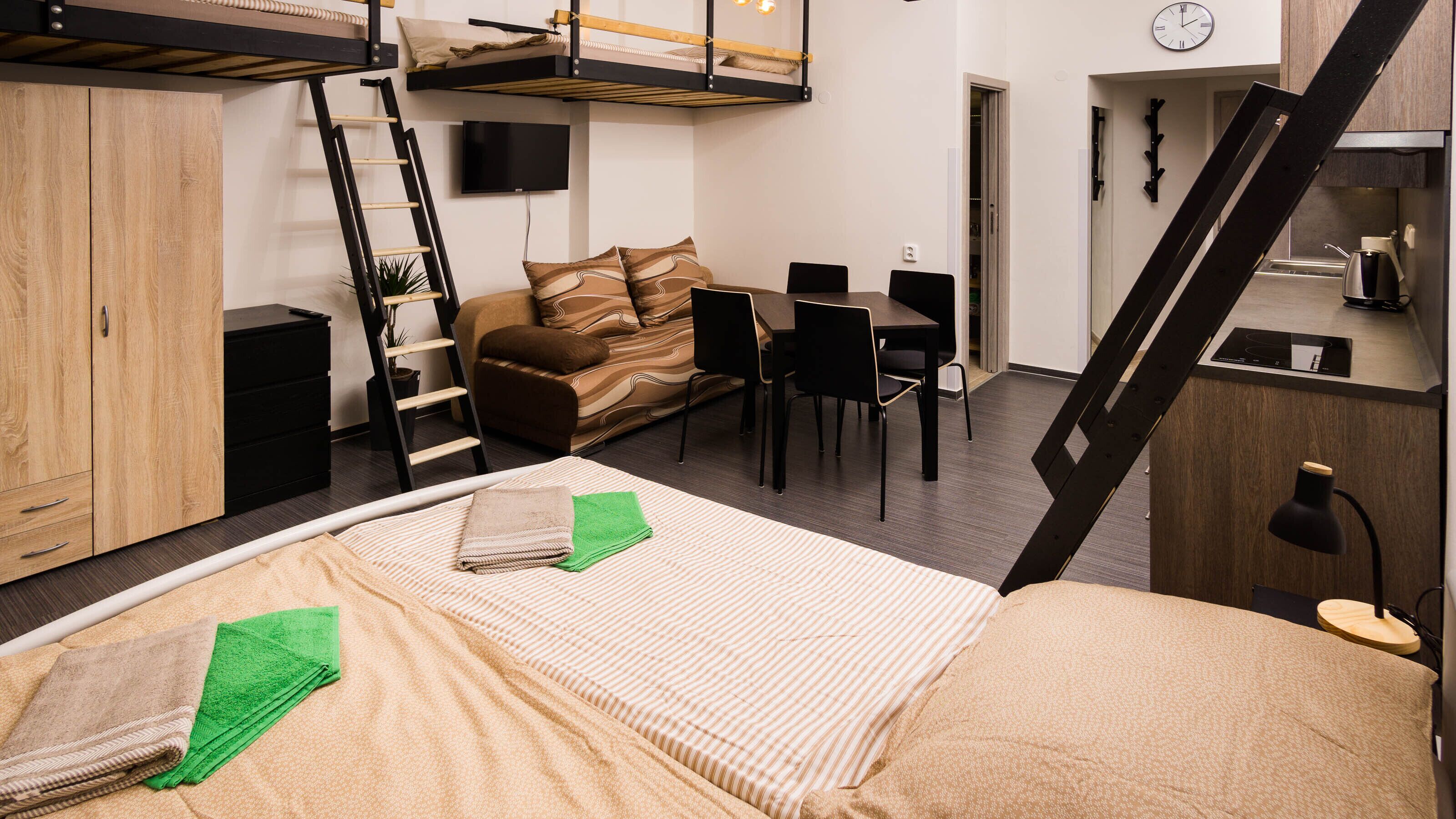A compact studio apartment with a loft bed, a dining area, a kitchenette, and a TV.