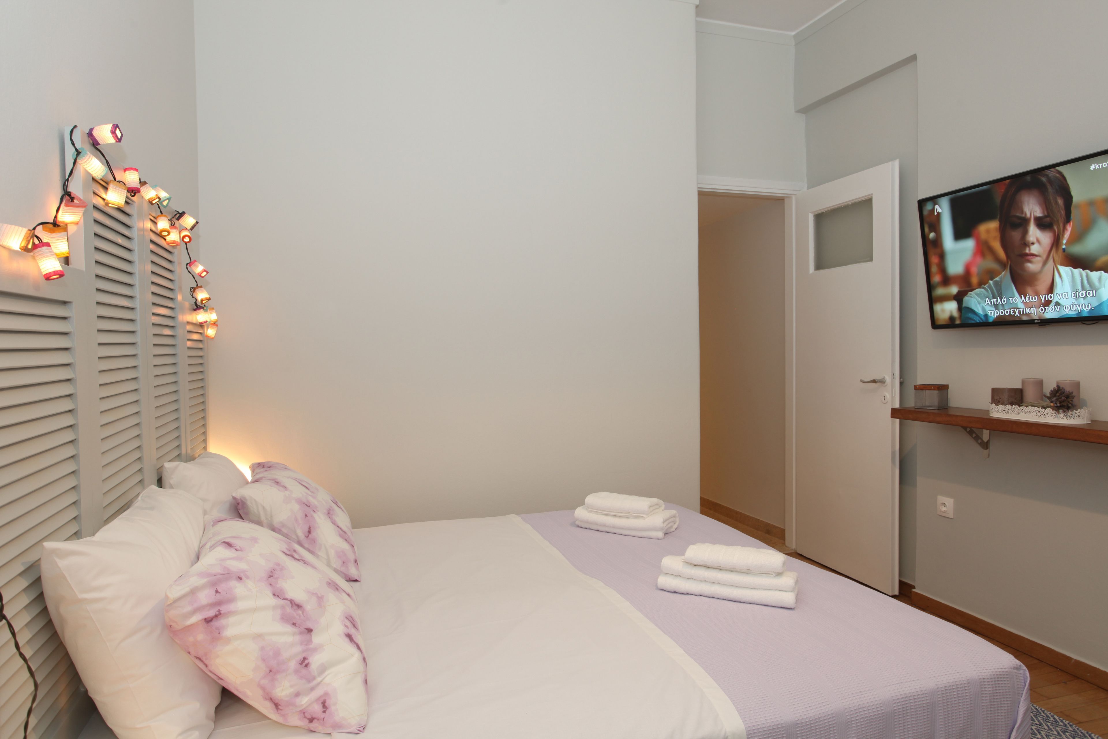 A bedroom with a bed, pillows, a TV, and a wall-mounted shelf.