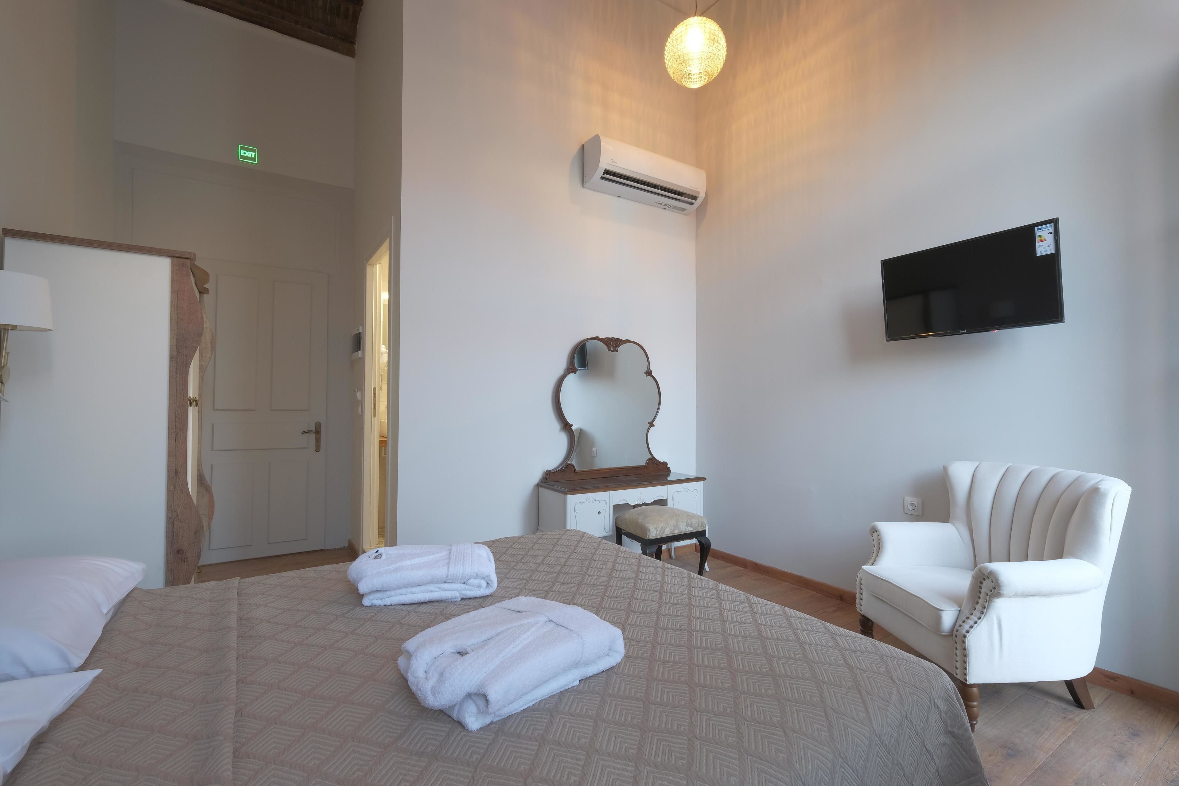Habitación de hotel con cama, silla, tocador con espejo, equipo de aire acondicionado y televisor de pantalla plana montado en la pared.