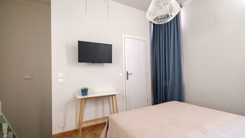 A bedroom with a bed, a TV mounted on the wall, a small table with a plant, and a door with curtains.