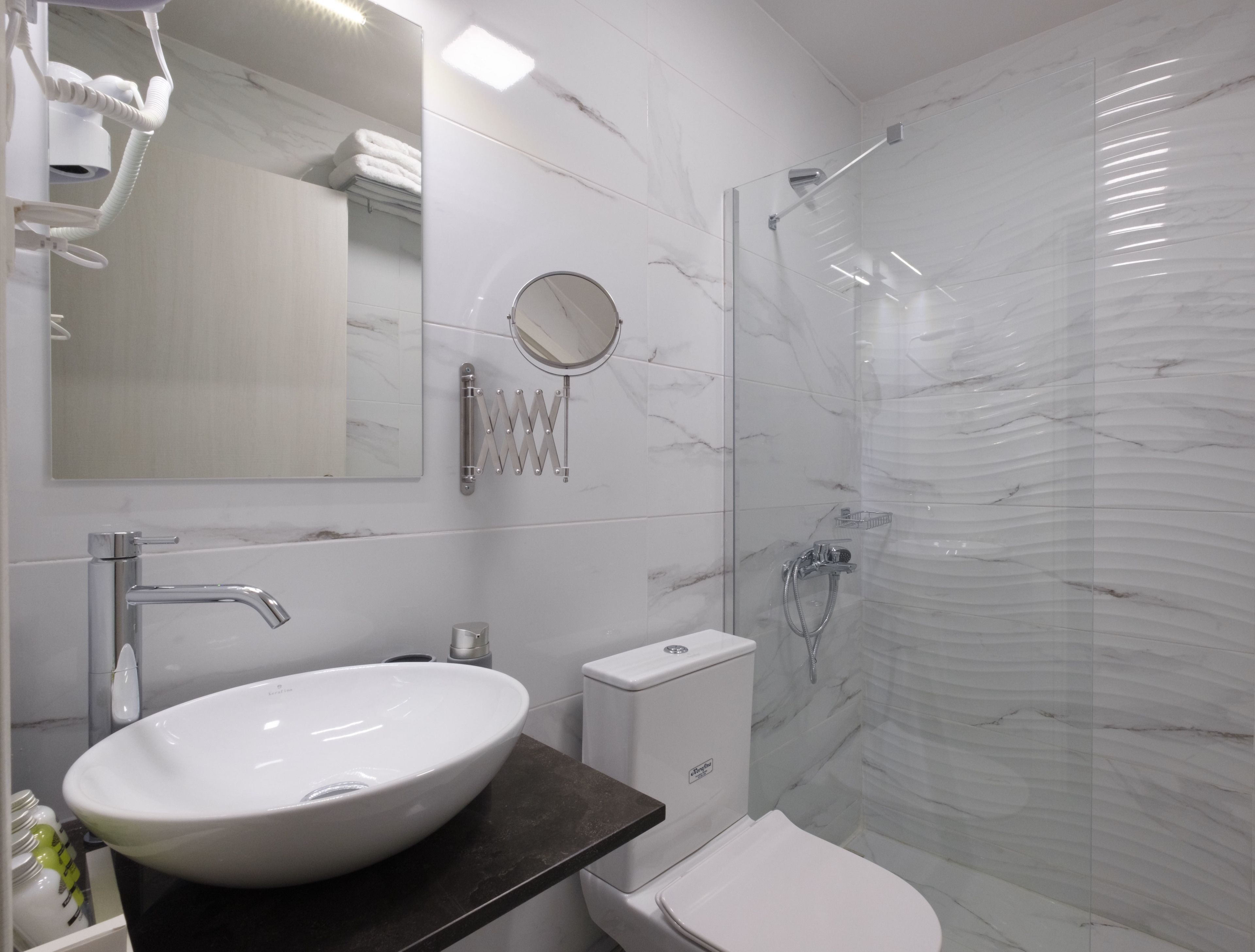 Un baño moderno con lavamanos blanco, espejo y cabina de ducha de vidrio.