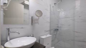 Un baño moderno con lavamanos blanco, espejo y cabina de ducha de vidrio.
