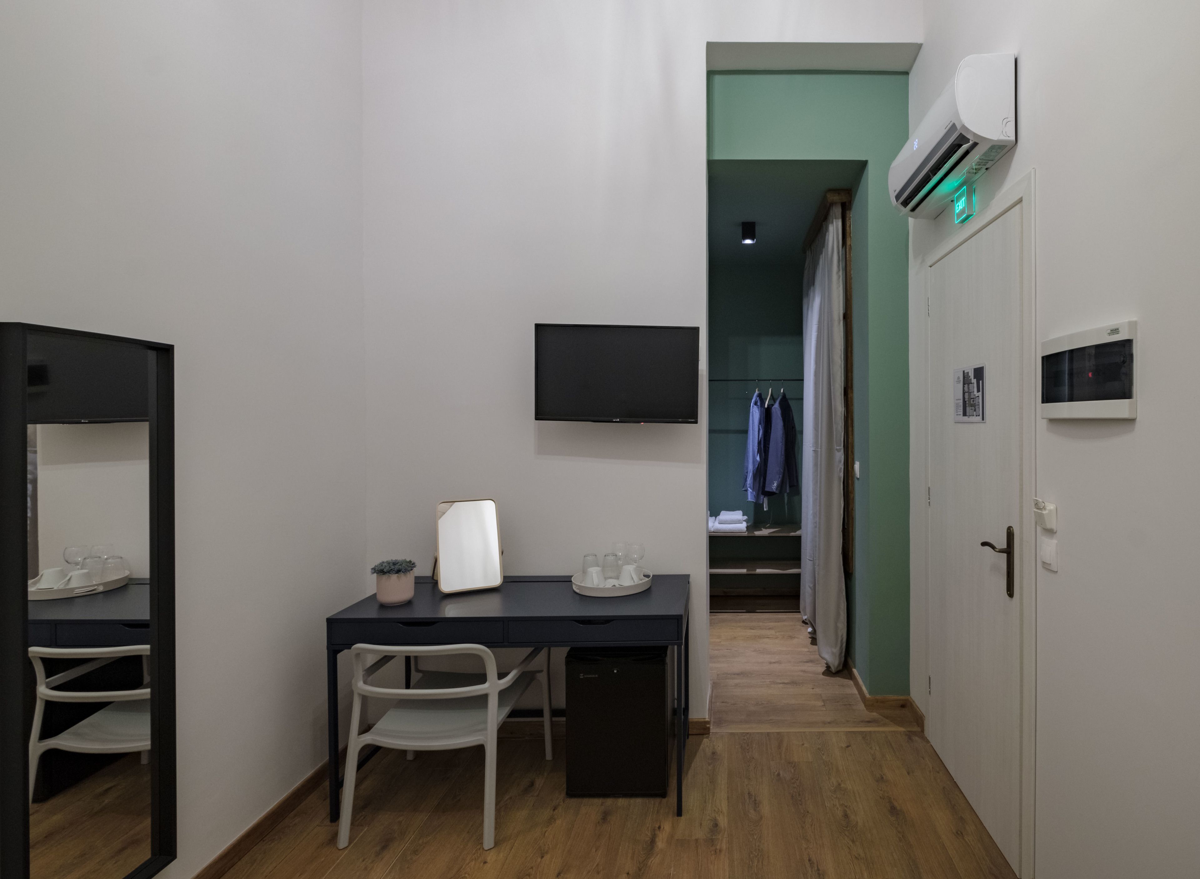 A compact hotel room with a desk, chair, and a flat-screen TV mounted on the wall.