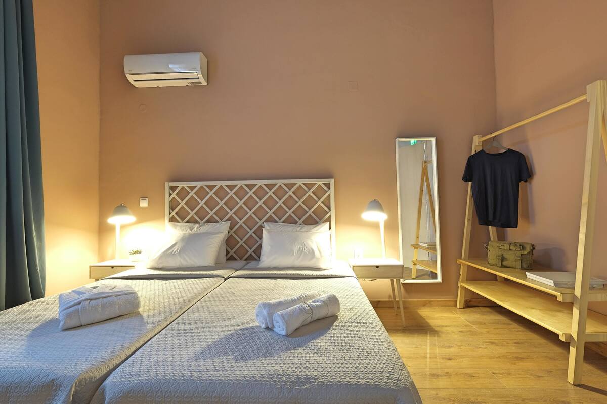A hotel room with two beds, a wardrobe, a mirror, and an air conditioning unit.