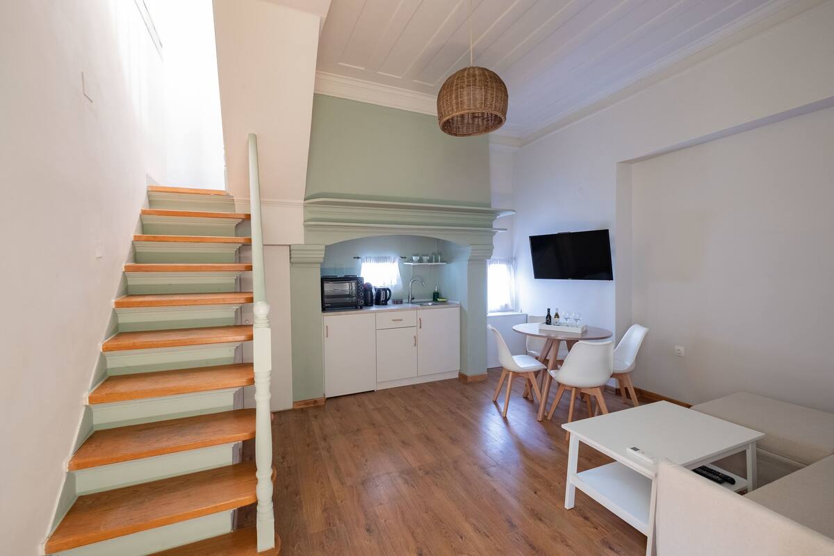 A modern kitchen with white cabinets, a dining area with a white table and chairs, and a staircase with wooden steps.