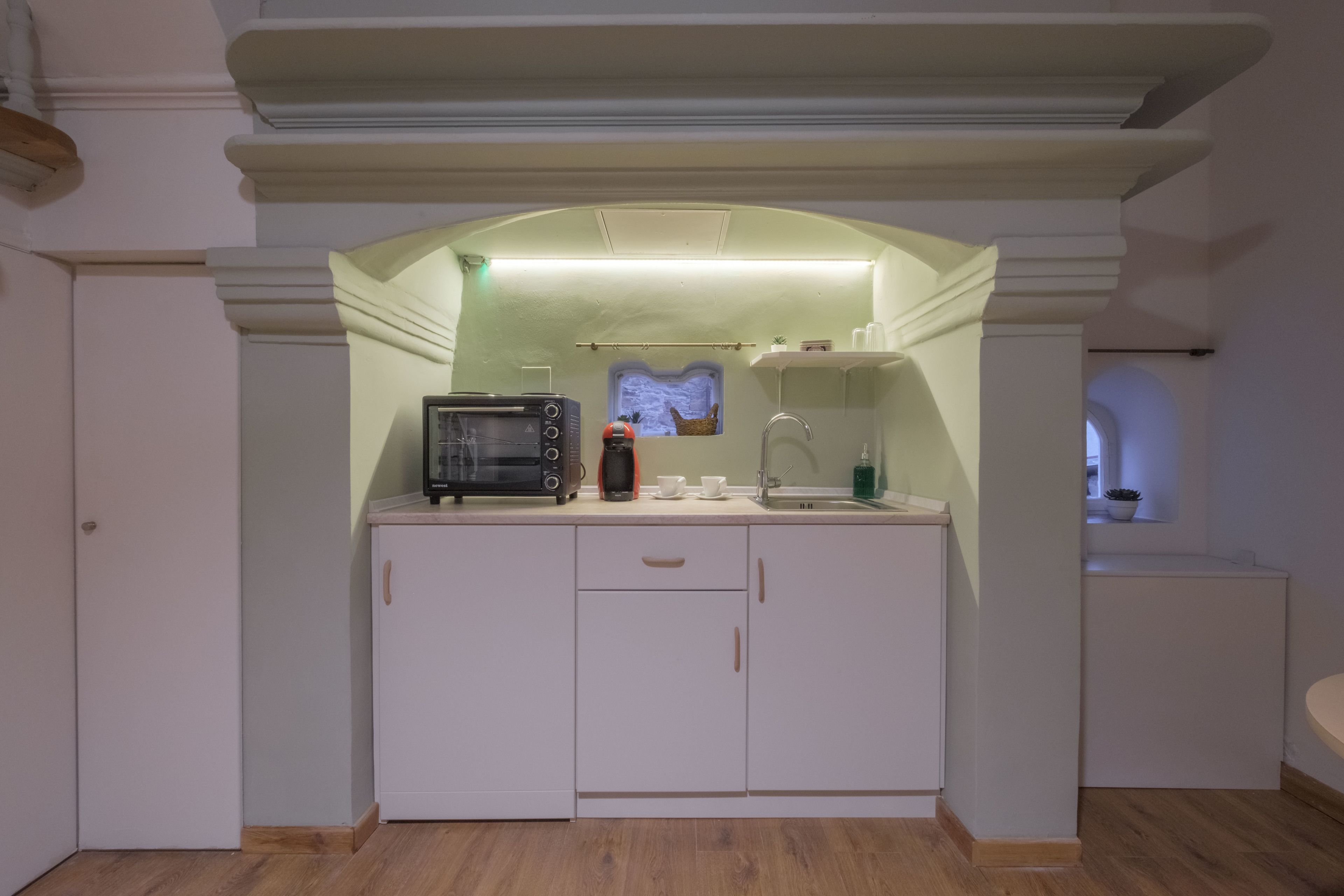 A compact kitchen with white cabinetry, a microwave, a coffee maker, and a small window above the sink.