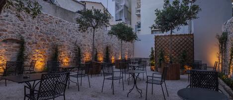 An outdoor seating area with tables and chairs, surrounded by stone walls and trees.