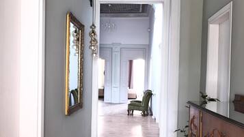 Um corredor com piso de madeira, um espelho grande e uma cadeira verde.