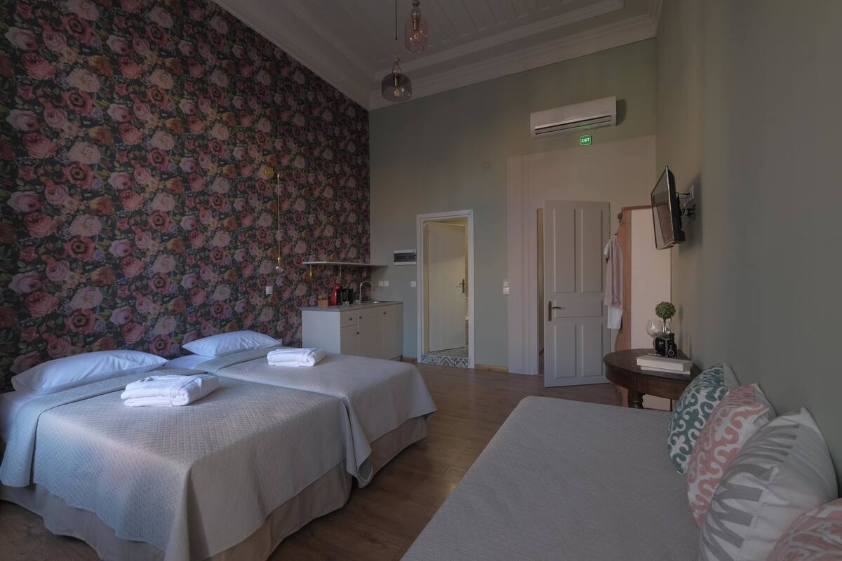 A hotel room with two beds, a desk, a chair, a small table, and a television.