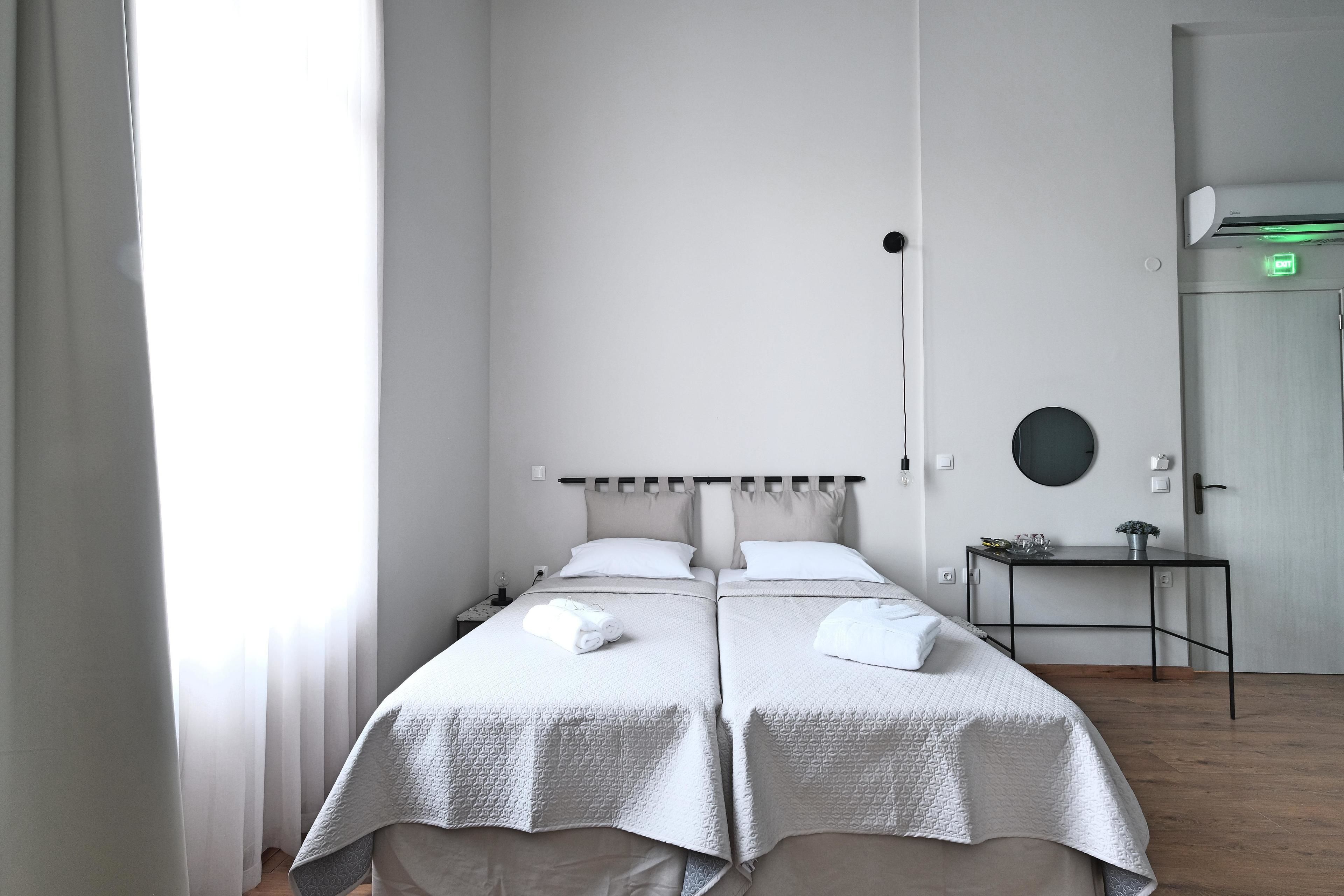 A hotel room with two beds, a bedside table, a round mirror, and a door with an emergency exit sign.