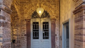 Un pasillo de piedra con arco, una lámpara decorativa, una puerta doble con paneles de vidrio y suelo de baldosas.