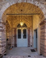 Un pasillo de piedra con arco, una lámpara decorativa, una puerta doble con paneles de vidrio y suelo de baldosas.