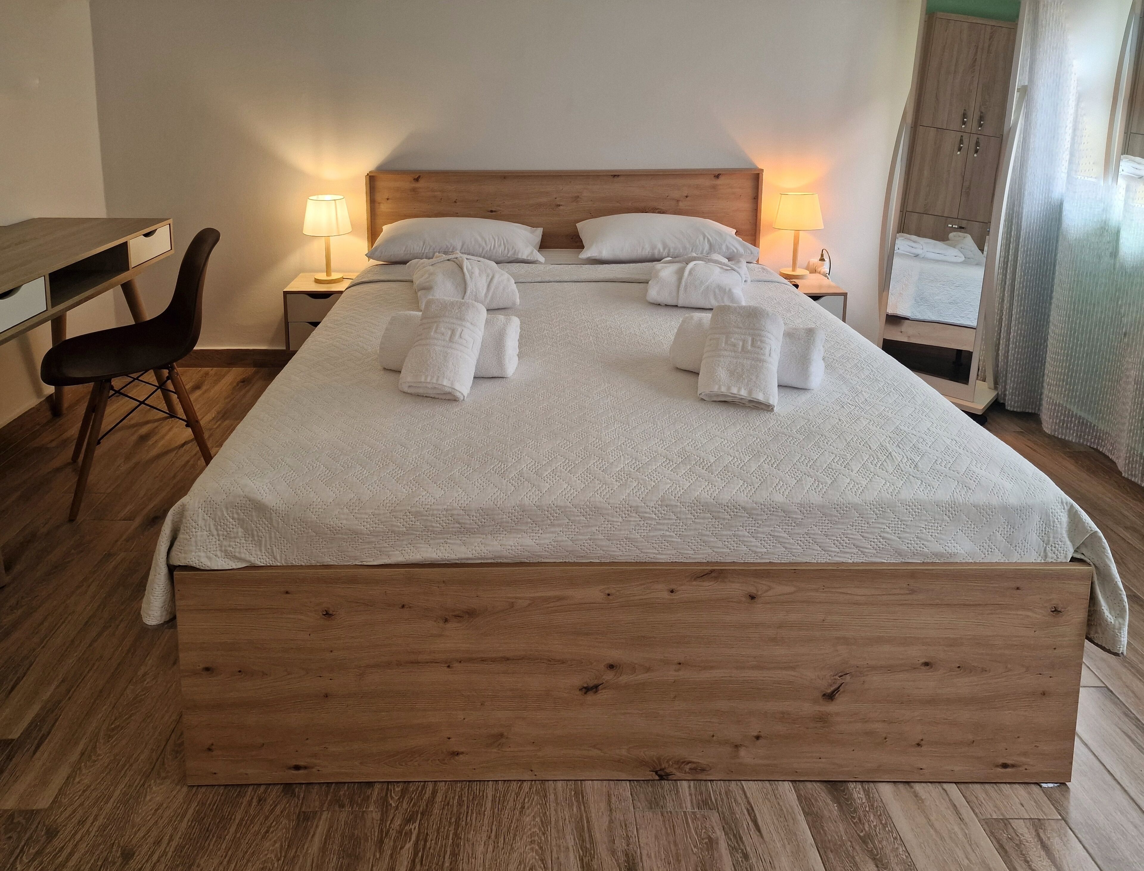 A neatly made bed with white linens and towels, a wooden headboard, and bedside lamps.