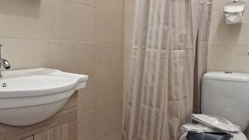 Een badkamer met een wit wastafel, houten kastje, douchegordijn, toilet en een handdoekdispenser.