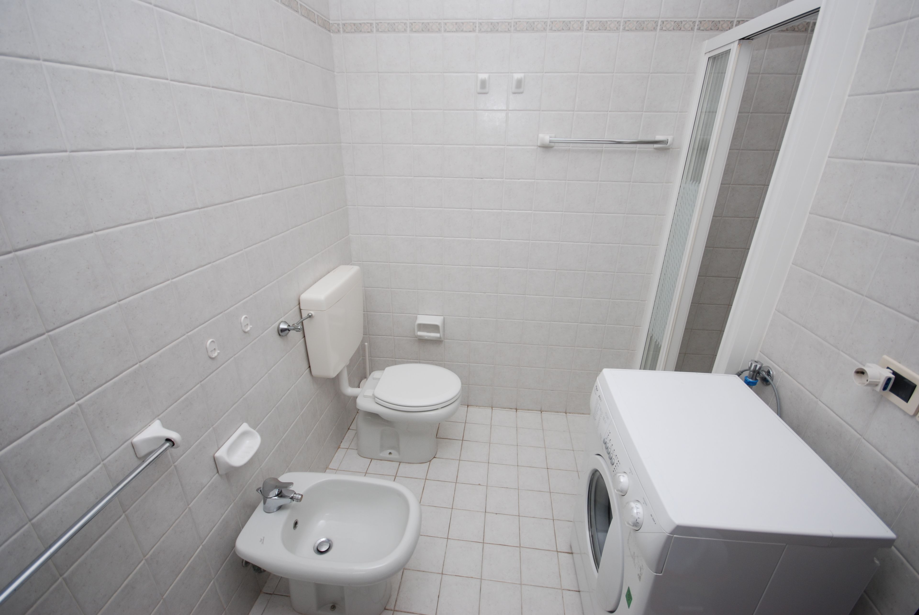 A small, white-walled bathroom with a toilet, bidet, and washing machine.
