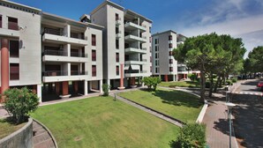 A modern apartment building with multiple balconies, a well-maintained lawn, and a clear sky. - Residence Porta del Mare (Lignano Sabbiadoro)