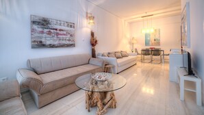 A modern living room with a beige sofa, a glass coffee table, and a dining area with a table and chairs. - L' apartment blanc dans le centre de Glyfada (Glyfada)