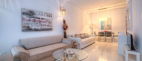 A modern living room with a beige sofa, a glass coffee table, and a dining area with a table and chairs.