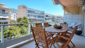 A balcony with a wooden table and chairs, overlooking a cityscape with buildings and trees. - L' apartment blanc dans le centre de Glyfada (Glyfada)