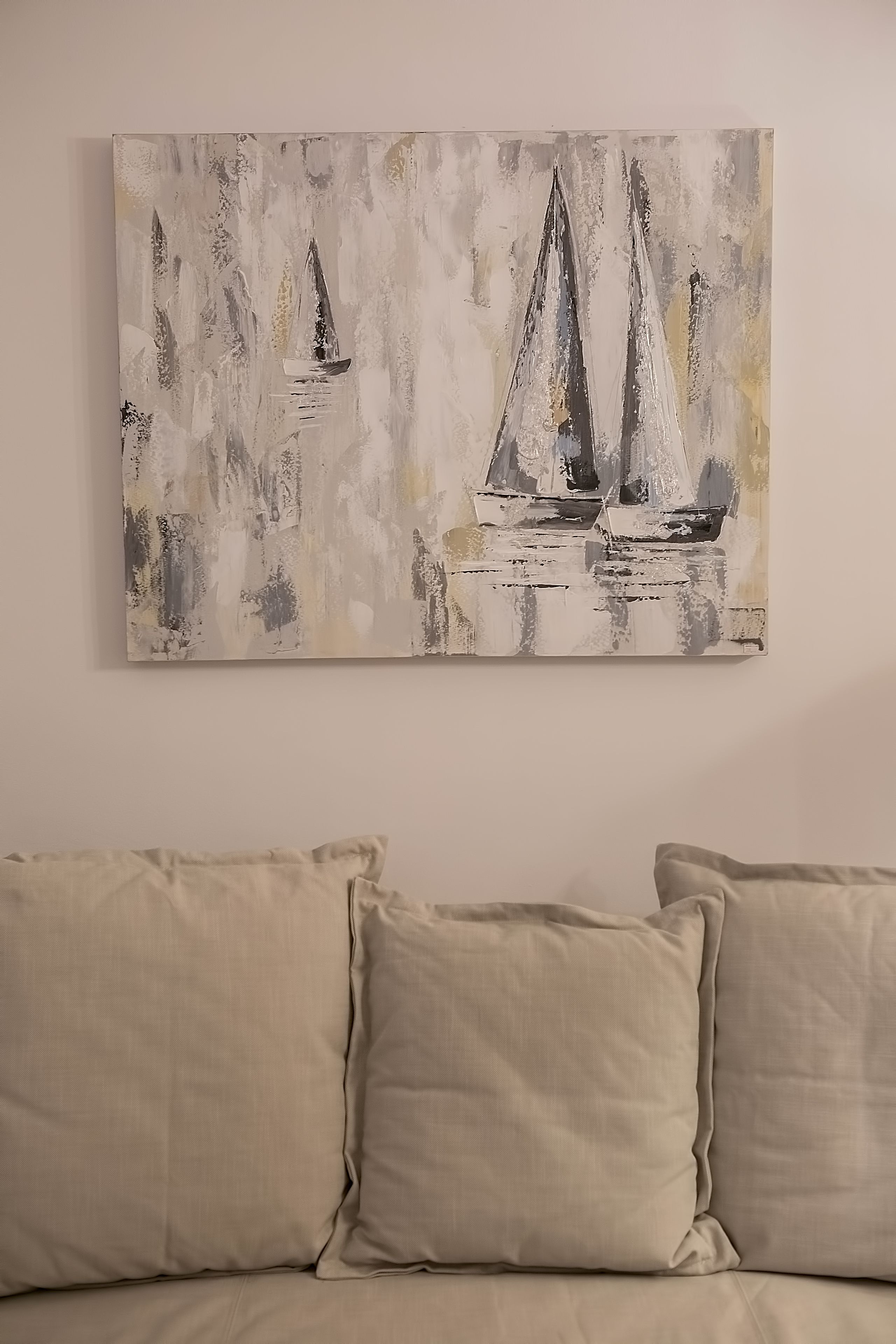 A painting of sailboats on a textured background, hung above a beige sofa with matching cushions.