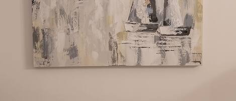 A painting of sailboats on a textured background, hung above a beige sofa with matching cushions.