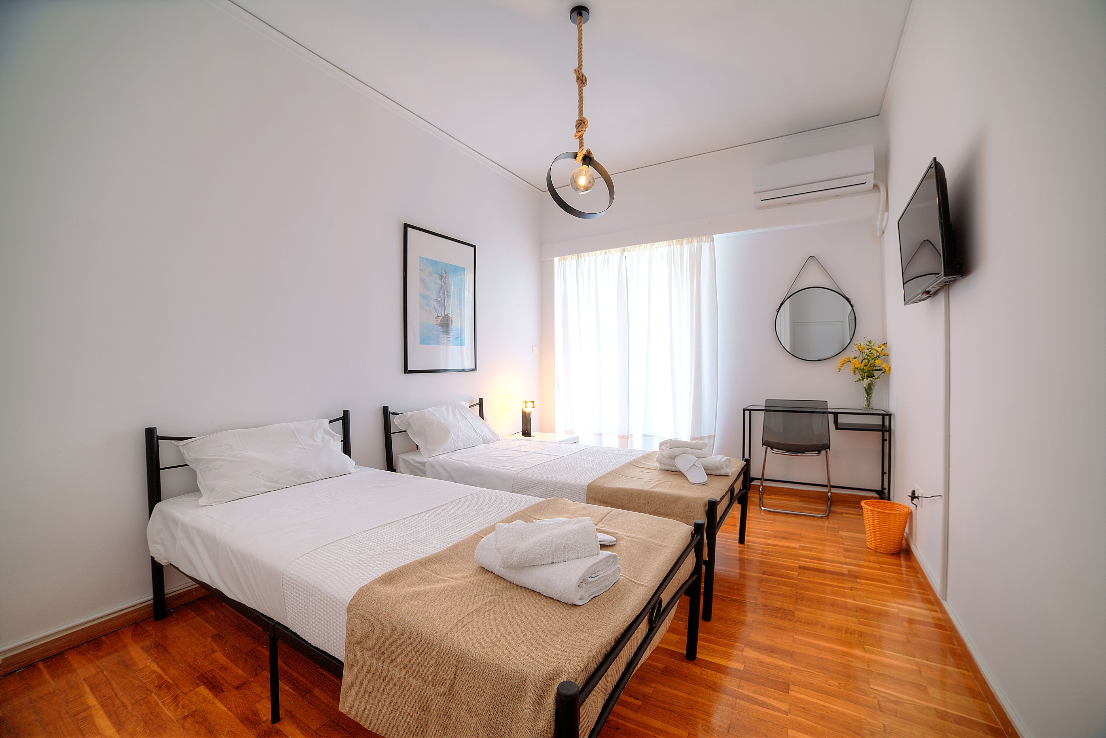 Habitació d'hotel amb dos llits, escriptori, cadira, televisió i finestra amb cortines.