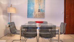 A dining area with a glass table, four chairs, a red bowl, a lamp, and a painting on the wall. - L' apartment blanc dans le centre de Glyfada (Glyfada)