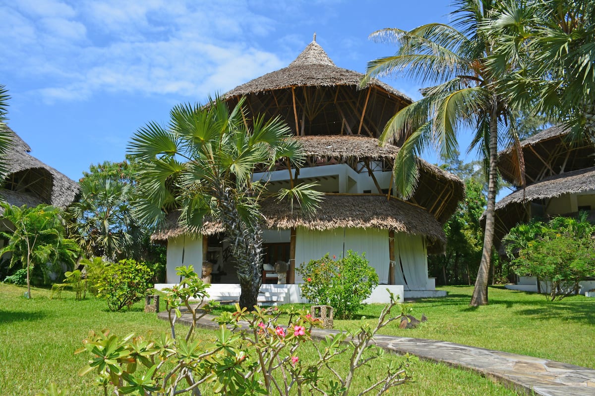 Ein Resort mit strohgedeckten Gebäuden, üppiger Vegetation und blauem Himmel.