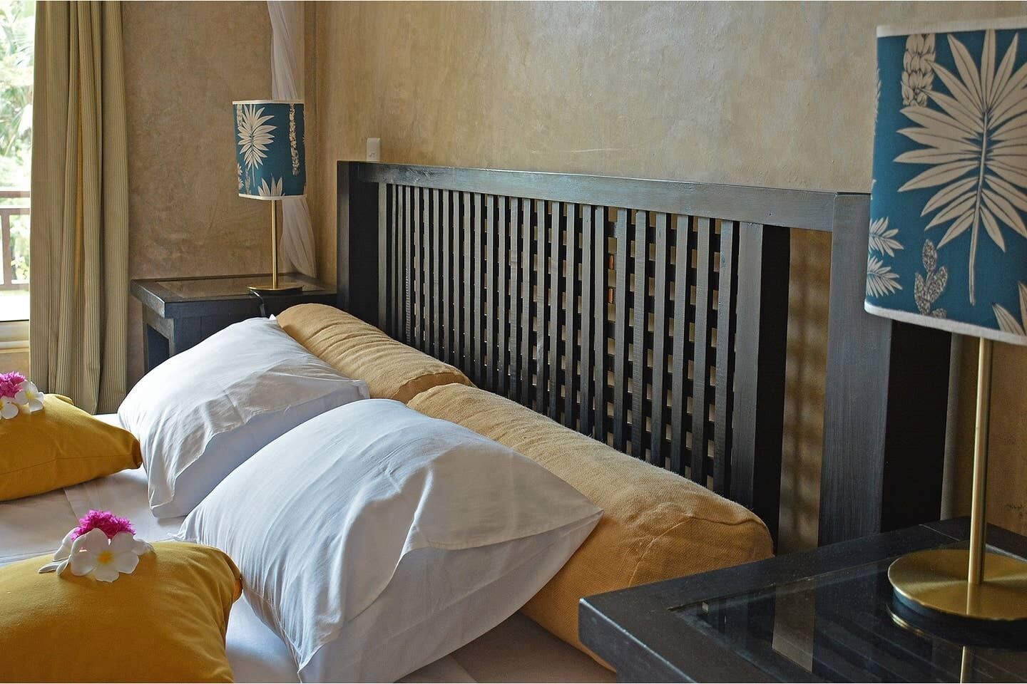 Hotellihuone, jossa on sänky, yöpöytä, lamppu ja koristeellinen seinäpaneeli.