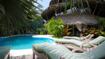 A pool area with lounge chairs and a thatched-roof structure.