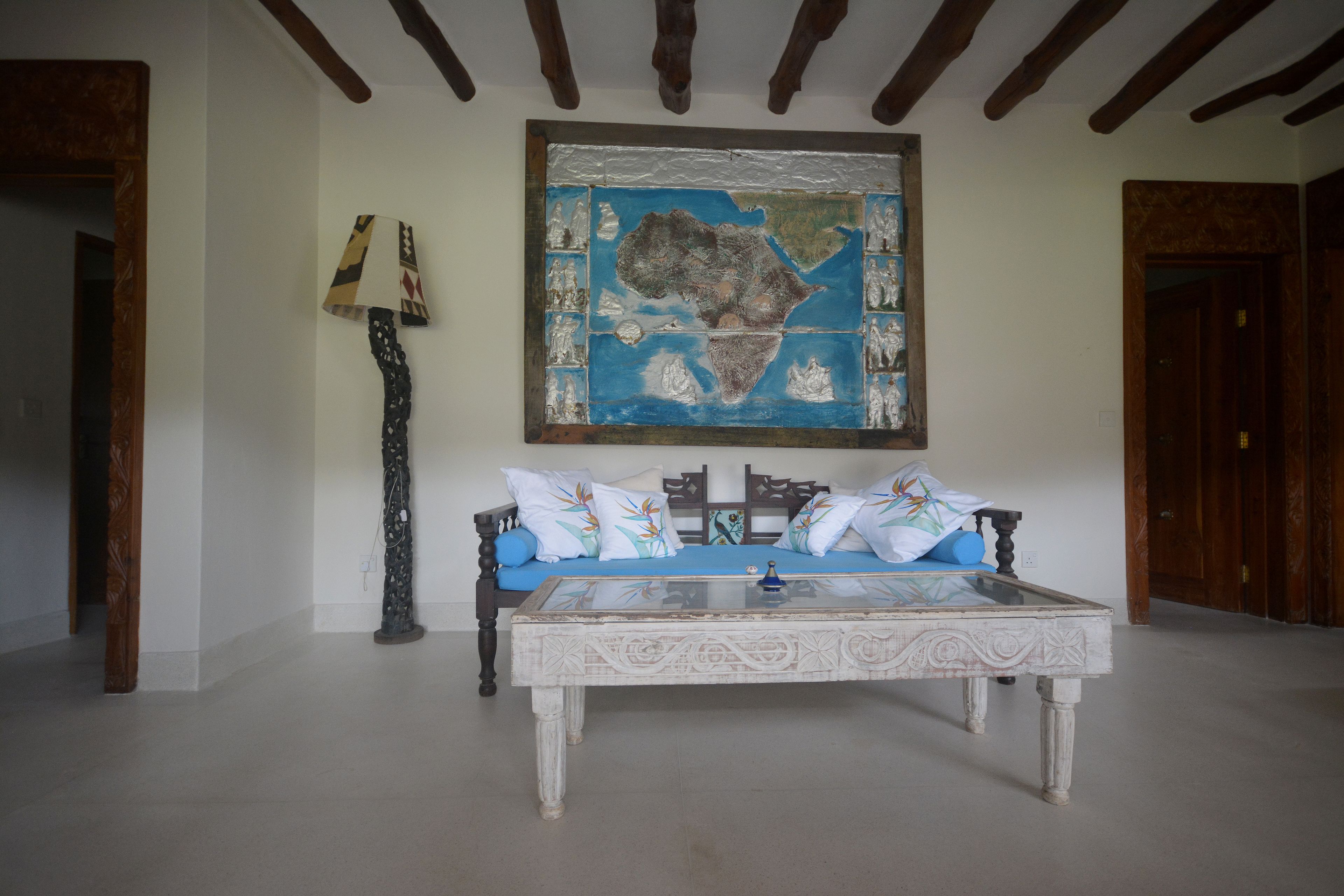 A room with a large map on the wall, a sofa with patterned cushions, and a tall floor lamp.